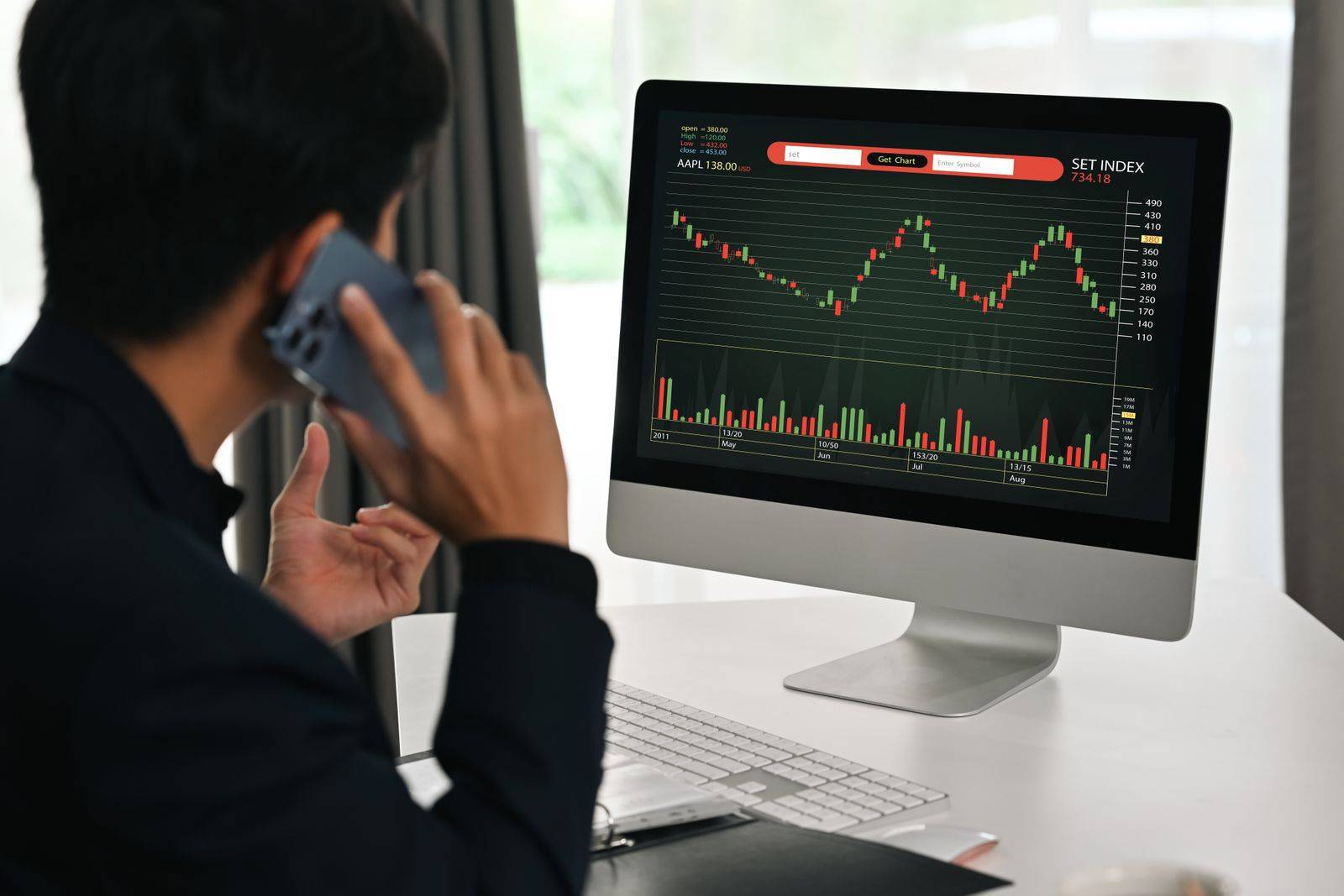 Back View Of Young Businessman Having Phone Conversation And Monitoring Stocks Data Candle Charts On Screen