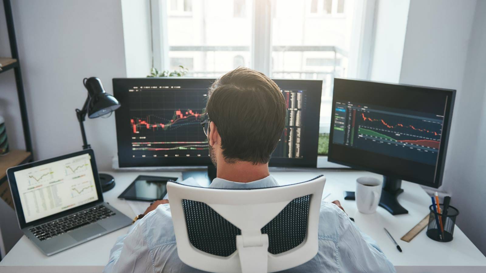 Back View Of Young Businessman Or Trader Working With Graph And Charts On Computers At His Modern Office