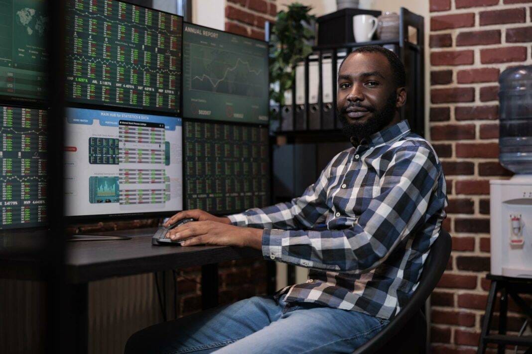 Confident Forex Stock Agent Sitting At Workstation With Multiple Displays Showing Real Time Financial Data.