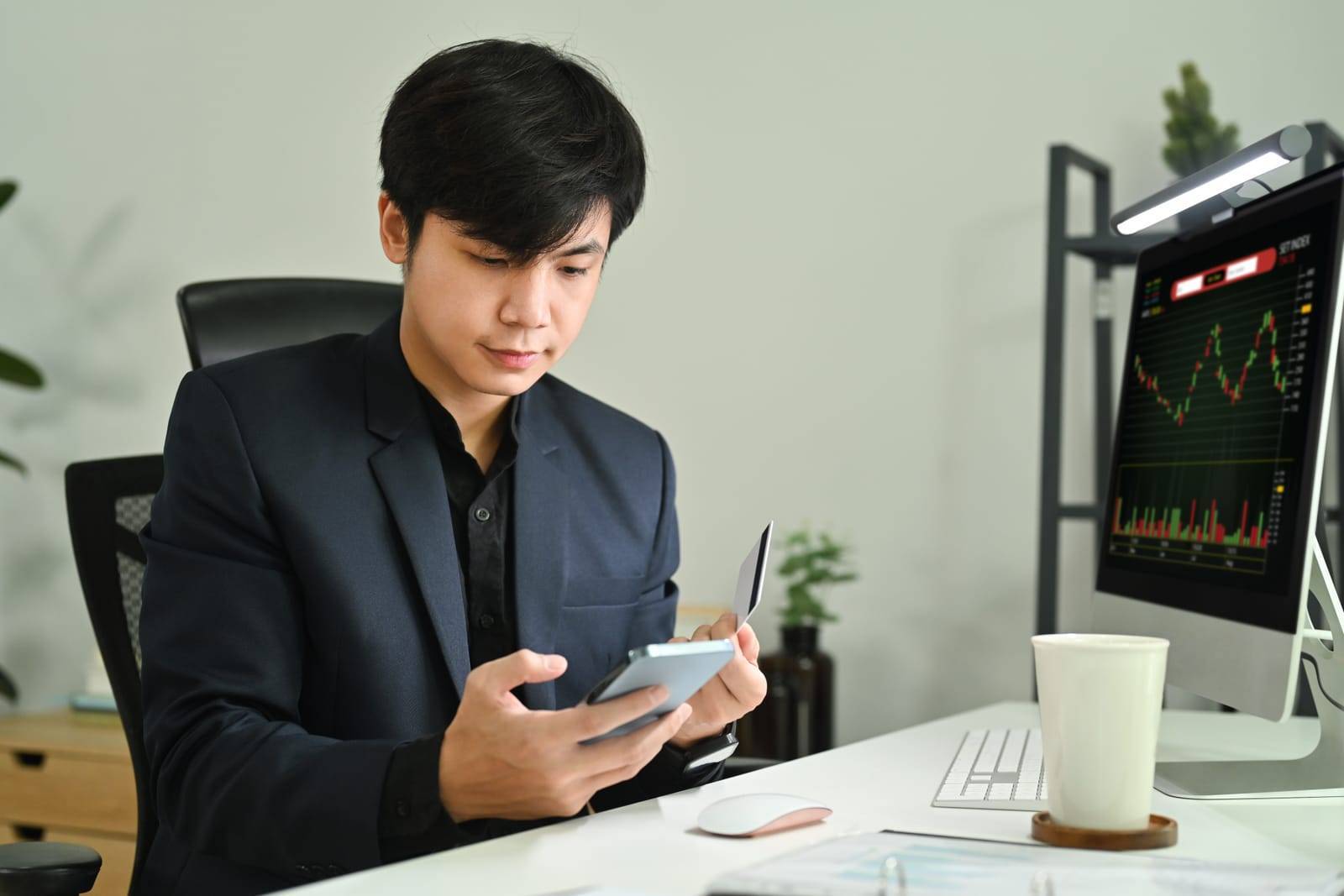 Male Financial Analyst Using Mobile Phone And Monitoring Stocks Data Candle Charts On Screen