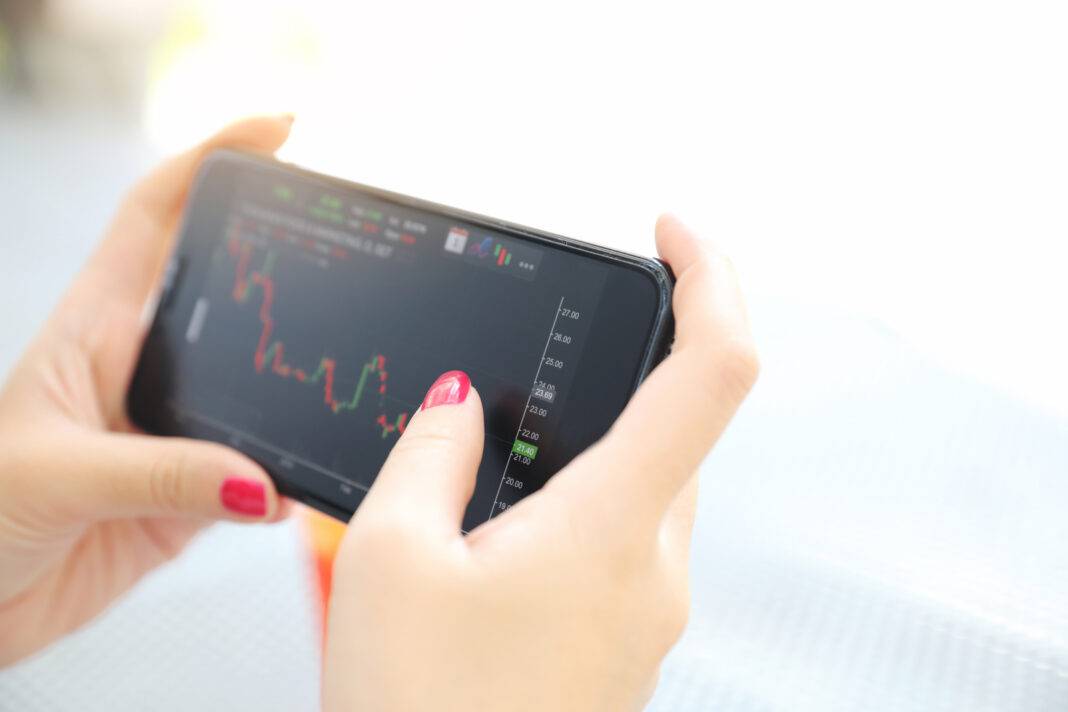 Female Hand With Smartphone Trading Stock Online In Coffee Shop