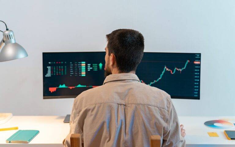 Rear View Of Young Caucasian Man Finance Broker Analyzing Stock Graphs While Trading From Home