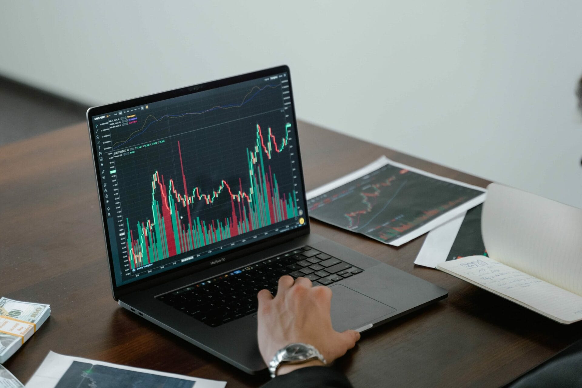 A trading graph and trends shown on a laptop and a printed copy on the tables with the money