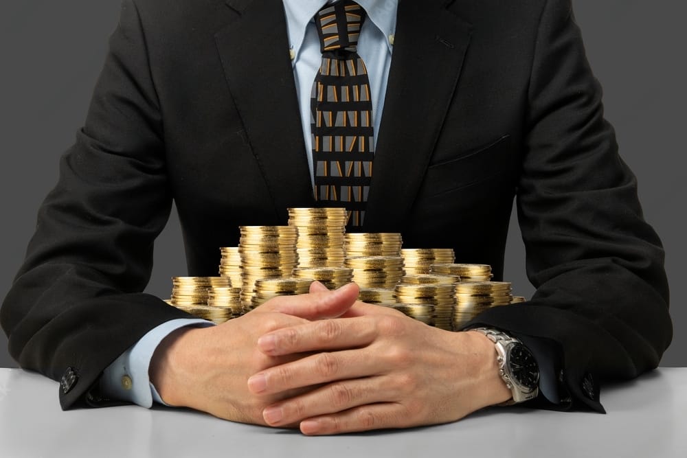 A businessmen in suit hugging a pile trading coins.