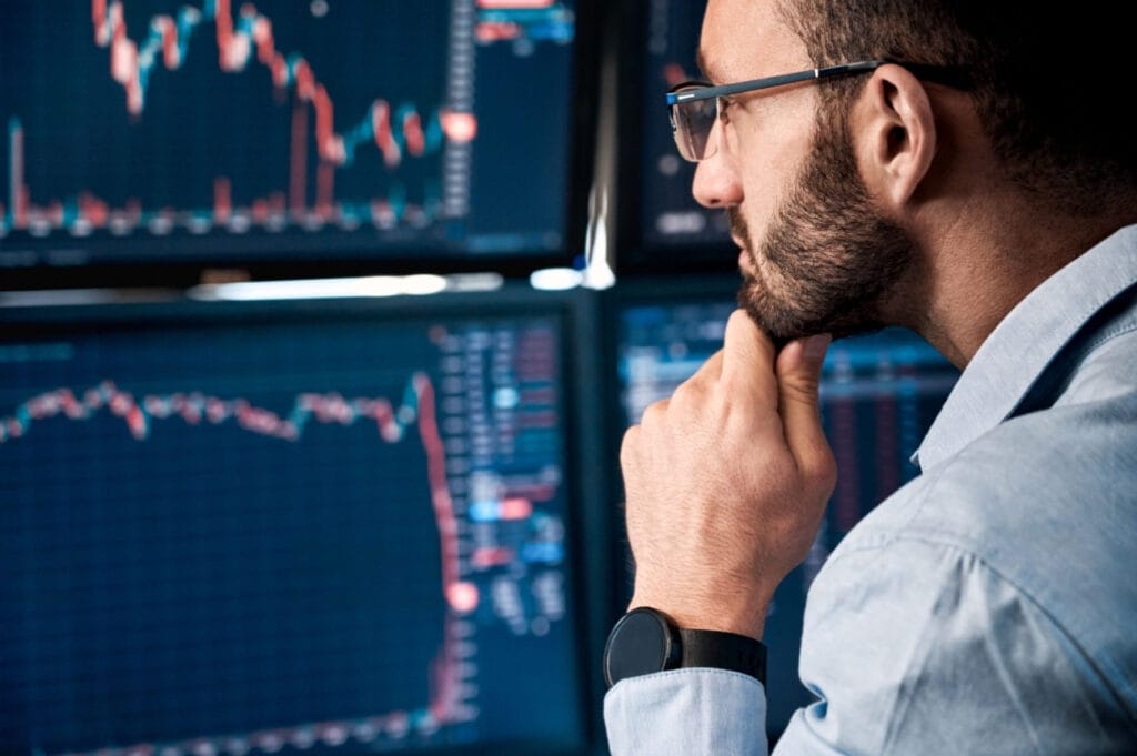 A man in suit understanding and comtemplating in front of a screen showing a candlestick graph.