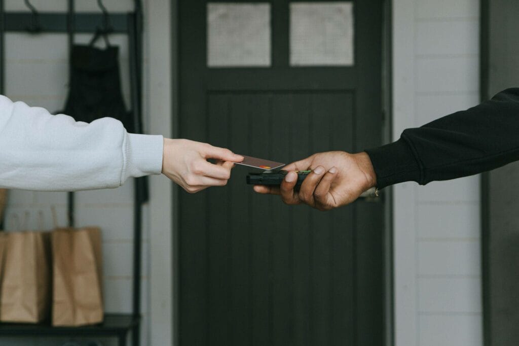 Arms meeting, one holding a bank card and the other a phone, indicating digital money transfer.