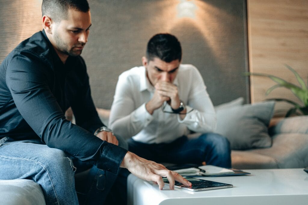 Two men in formal attire analyzing a candlestick stock graph, contemplating crypto-related issues.